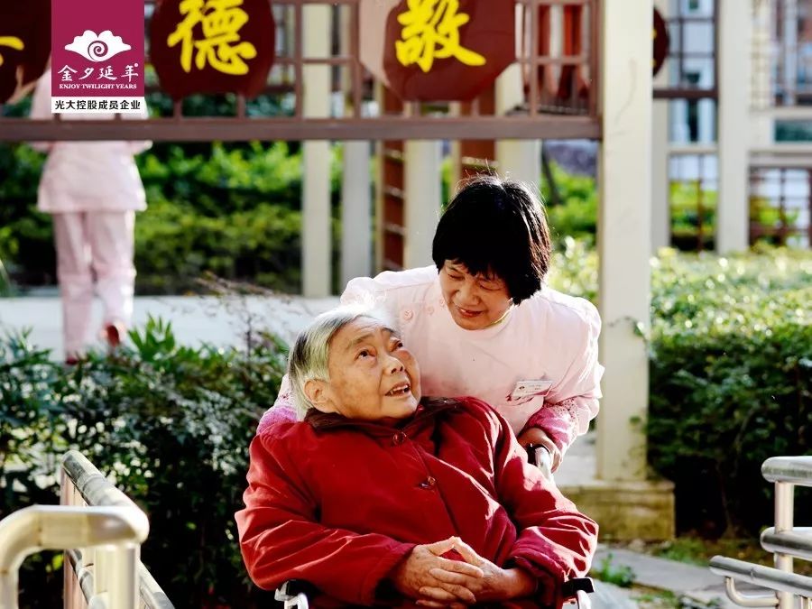 春日暖阳，两女子推护理床上的老人赏花